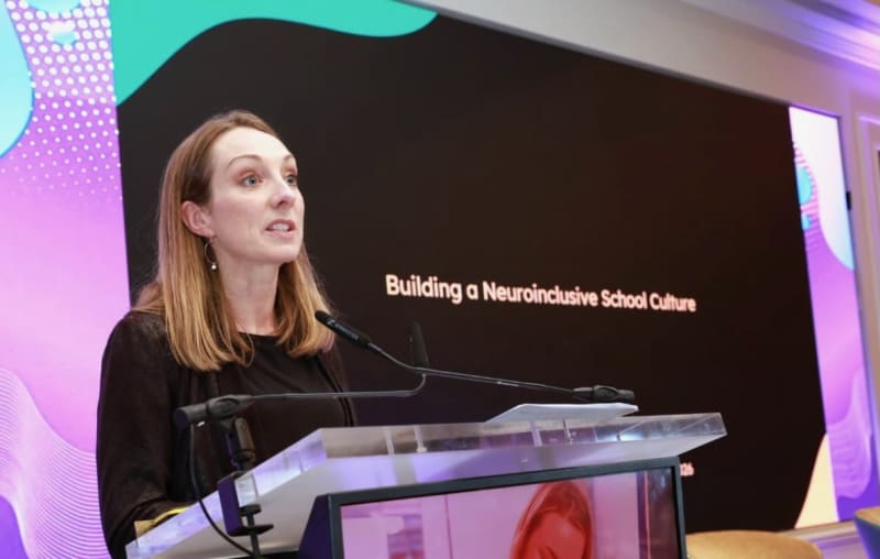 Sarah Colgan speaking at a podium during a presentation titled Building a Neuroinclusive School Culture.