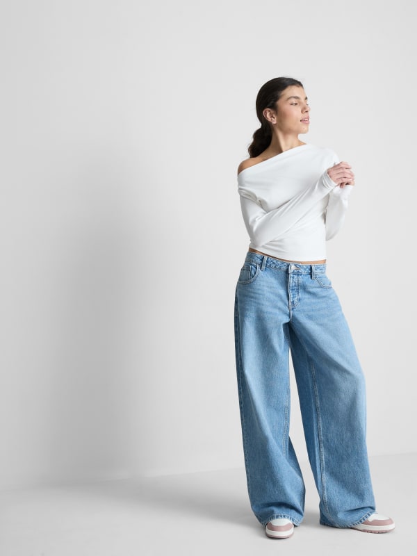 Woman wearing a white off-shoulder wrap crop top and wide-leg light blue jeans with white sneakers.