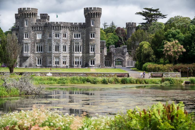 Johnstown Castle, a Gothic Revival stone castle with battlemented towers reflected in a foreground pond, County Wexford, Ireland.