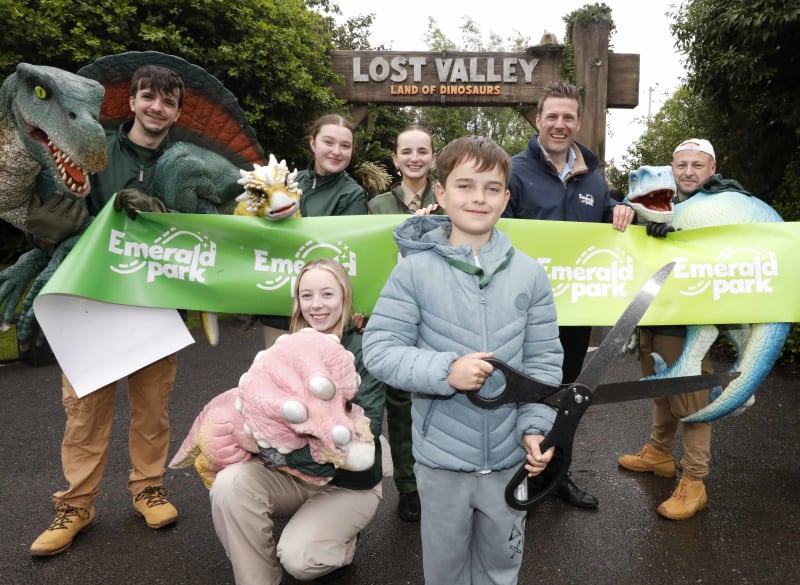 Group ribbon-cutting ceremony at Lost Valley Land of Dinosaurs entrance at Emerald Park with children and staff.