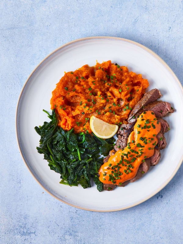 Rump steak with cowboy butter sauce, sweet potato mash and wilted spinach on a white plate.