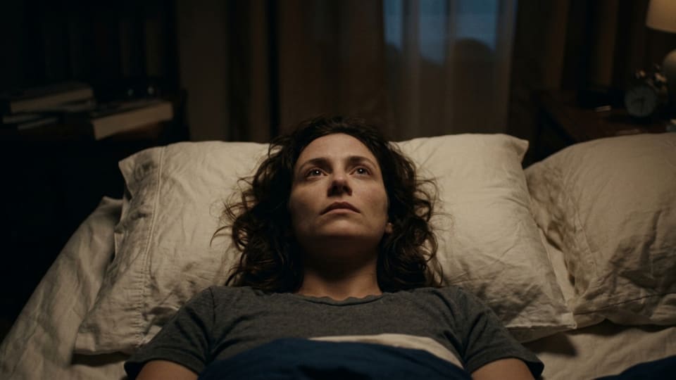 lady lying in bed with eyes open staring at the ceiling. dim light