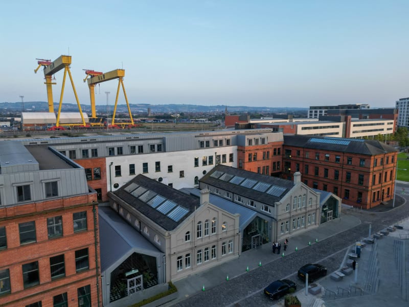 Aerial view of Belfast's Titanic Quarter with yellow Harland & Wolff cranes and restored Victorian buildings.