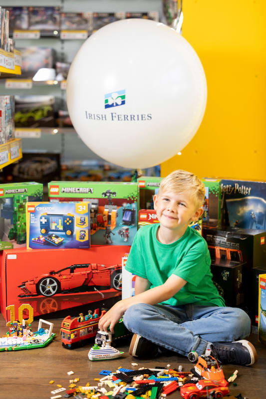 Theo Ducey, age 6, sits surrounded by LEGO sets and an Irish Ferries balloon, holding a small LEGO ferry model.