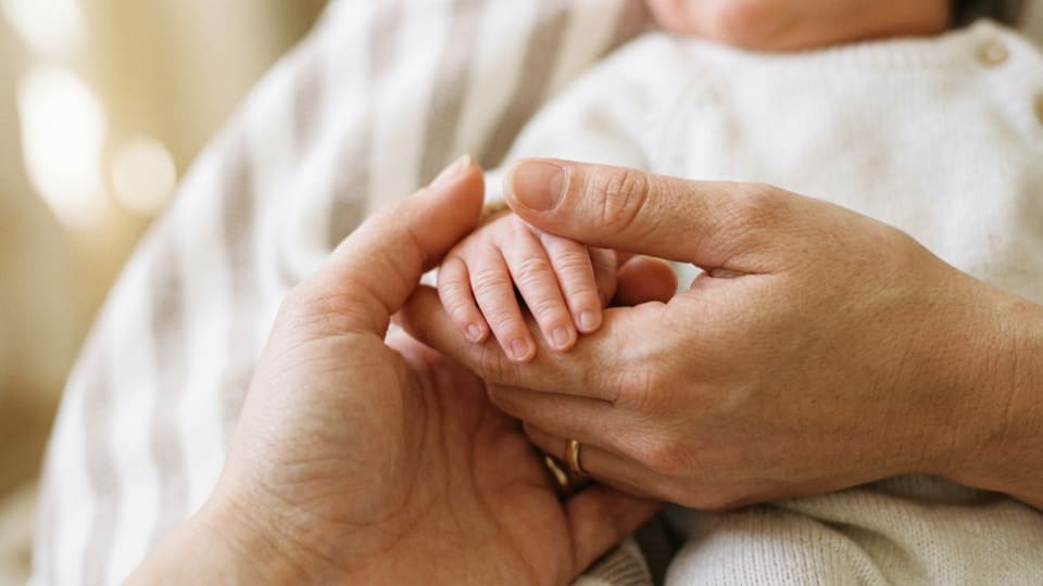 A close-up of a parent's hand holding a tiny newborn baby's hand, soft warm tones, intimate and tender atmosphere