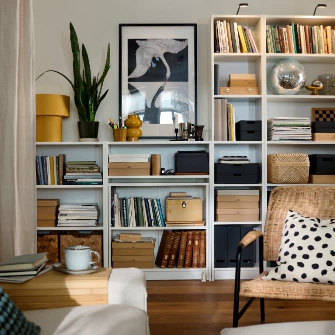 White modular shelving units styled with books, storage boxes, plants, and decor in a cosy living room.