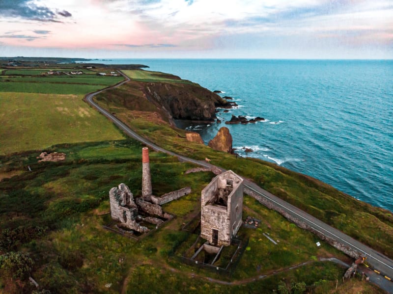 Aerial view of ruined coastal mine engine houses with chimney on a green clifftop at dusk, Ireland.