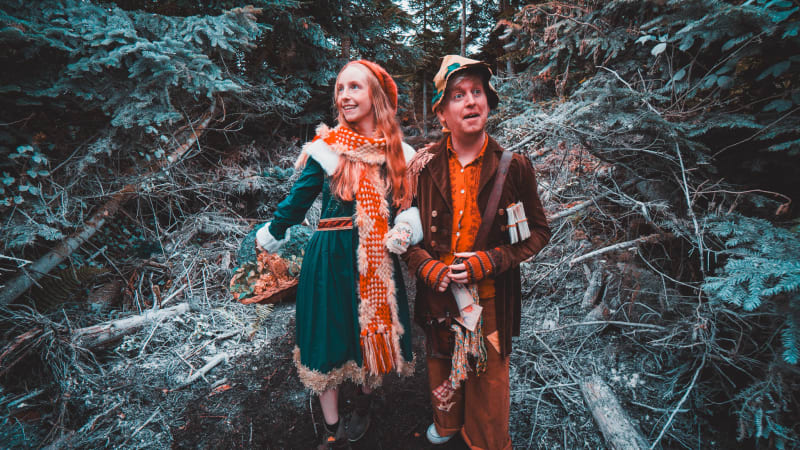 Fiadh and Nollaig in theatrical folk costumes standing among fallen pine trees in a forest.