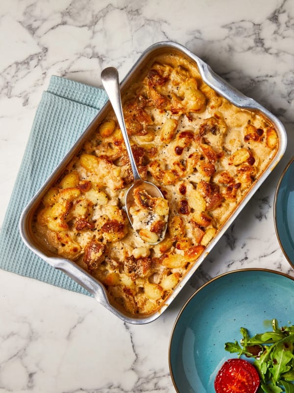 Baked gnocchi cacio e pepe with golden crust in a silver roasting tin, served with a spoon.