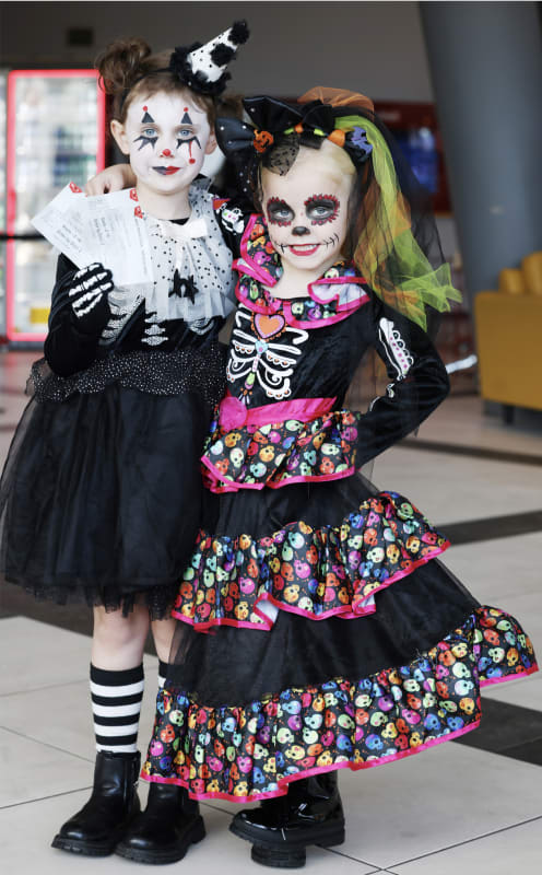 Two girls in Halloween costumes — one as a clown, one in a Day of the Dead sugar skull outfit with face paint.