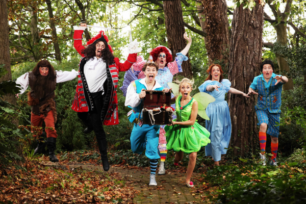 Seven performers in colourful pantomime costumes posing on a woodland path with a treasure chest.