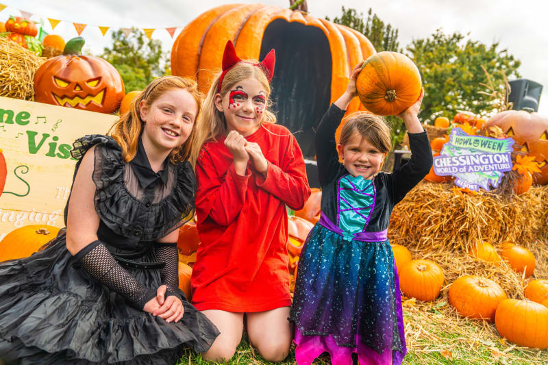 Three children in Halloween costumes at Chessington World of Adventures Howloween event with pumpkins and hay bales.