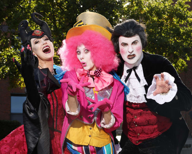 Three performers in Halloween pantomime costumes: a villain, Mad Hatter, and vampire, posing dramatically outdoors.