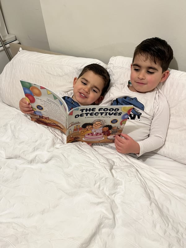 Two young boys in dinosaur pyjamas reading 'The Food Detectives: A Gluten-Free Mystery' in bed.
