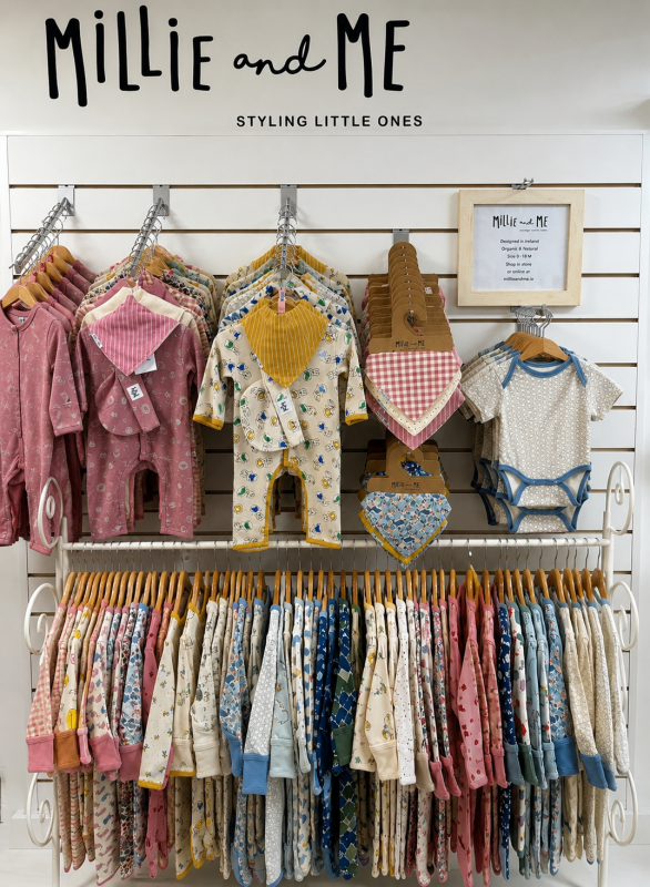 Millie and Me baby clothing display wall with organic sleepsuits, rompers, bibs and bodysuits in pink, blue and cream.