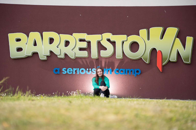 Kaela Nolan sitting in front of the Barretstown 'a serious fun camp' wall sign.