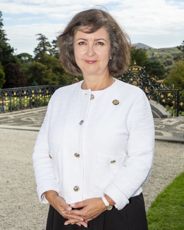 Zuzana Vatralova, IOM Ireland Chief of Mission, standing outdoors in a white jacket with UN SDG pin badge.