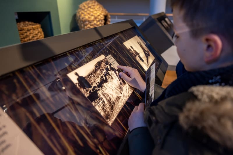Young boy interacting with backlit black-and-white photo panels at a museum exhibition display.