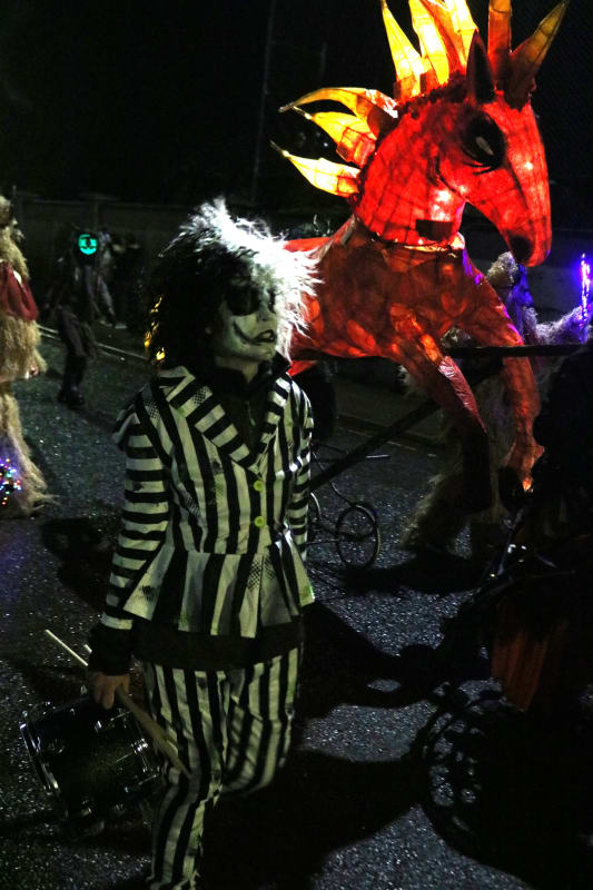 Child in Beetlejuice costume with face paint at a night parade beside a large illuminated red dragon lantern.